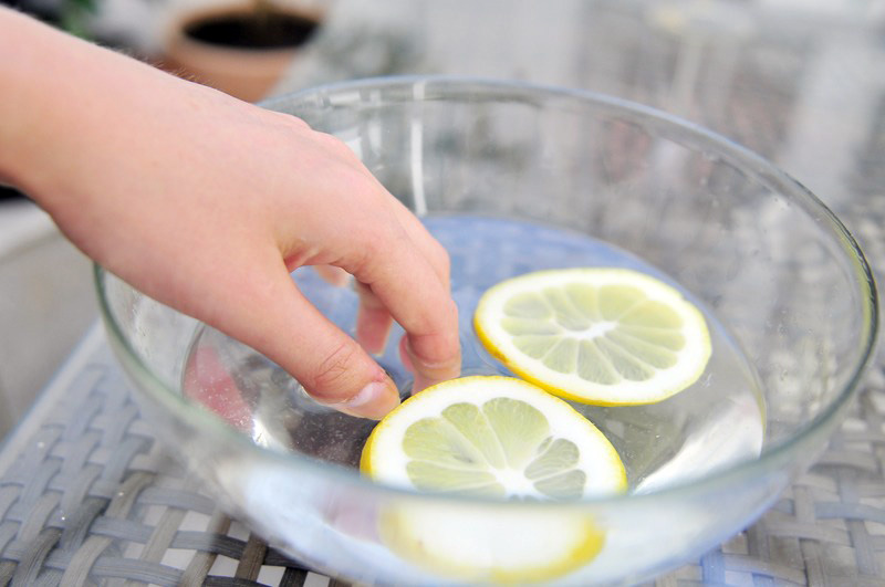 تصویر قرار دادن دست در محلول آب و لیمو برش خورده برای زیبایی در آشپزخانه
